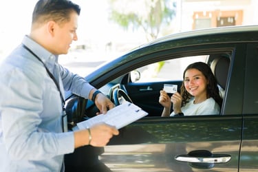 driving instructor standing outside window of car talking to teen driver holding new license