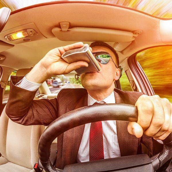 Image of a man driving and drinking from a flask Image of a man driving and drinking from a flask