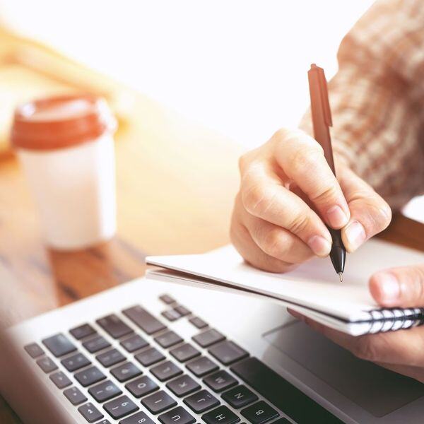 someone taking notes on paper looking at a laptop
